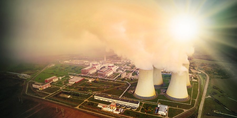 Aerial view to nuclear power plant in industrial landscape. Radiation and air pollution theme. Warm filtered picture.